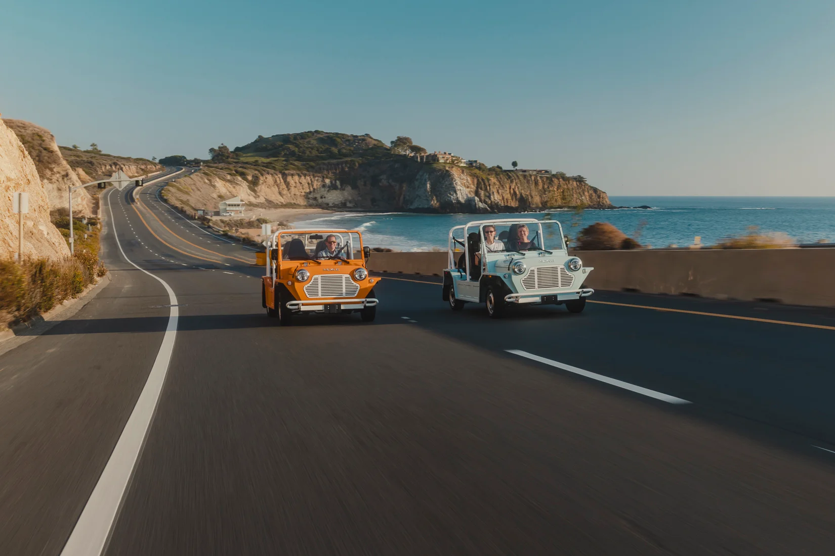 Two electric Mokes driving up the Pacific Coast Highway past Laguna Beach