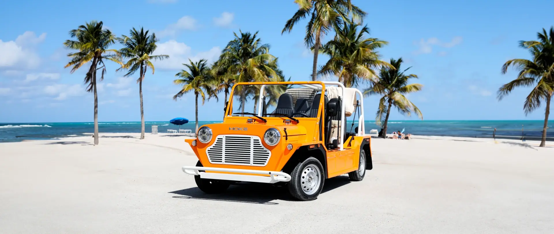 Open-air Moke EV driving along a lush Hawaiian coastal road at golden hour