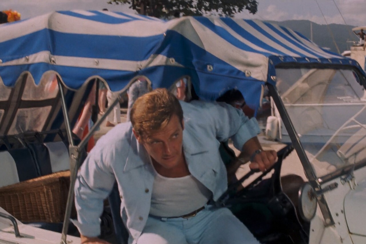 Roger Moore as James Bond driving a Mini Moke on a tropical island set, from a Bond film